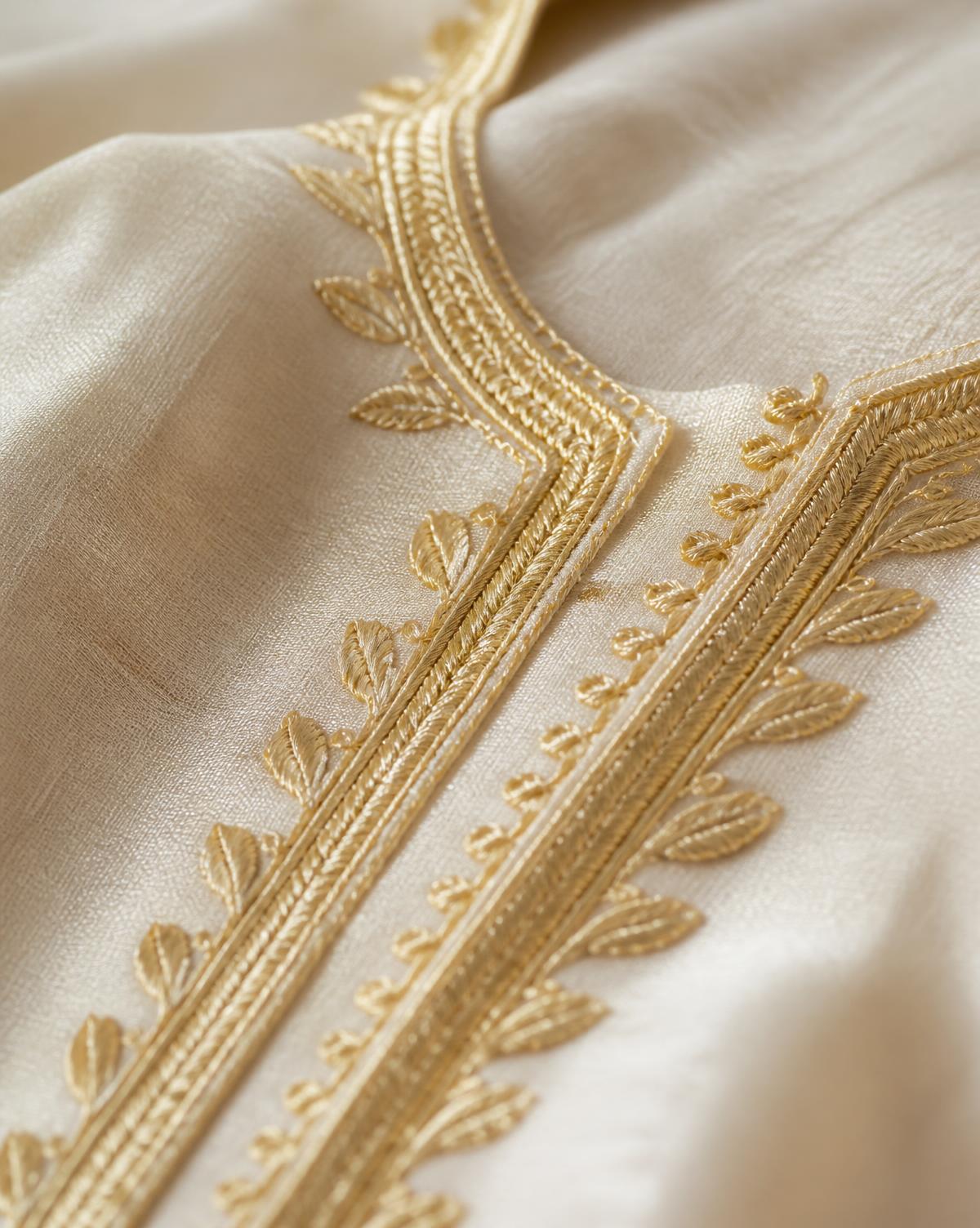 Macro-detail van handgeborduurd gouddraad op ivoren sabra-zijde van een Marokkaanse caftan